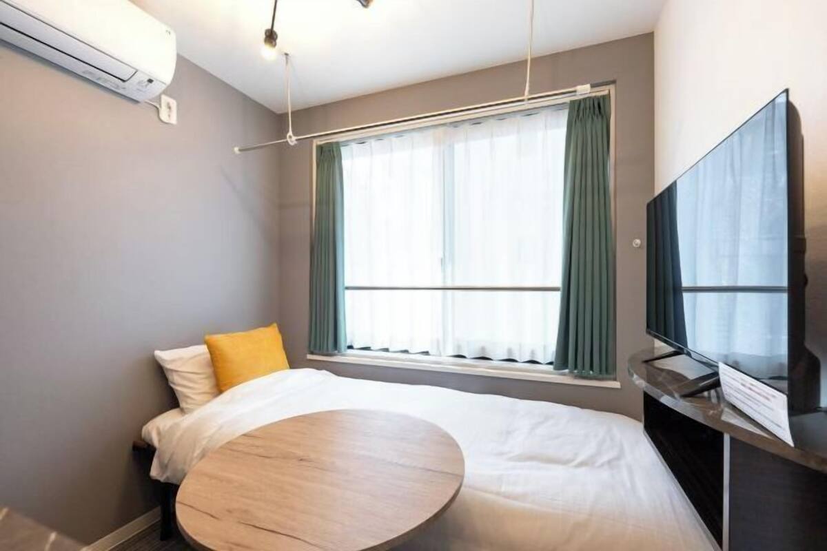 A hotel room with a bed, a round table, a TV, and a window with curtains.