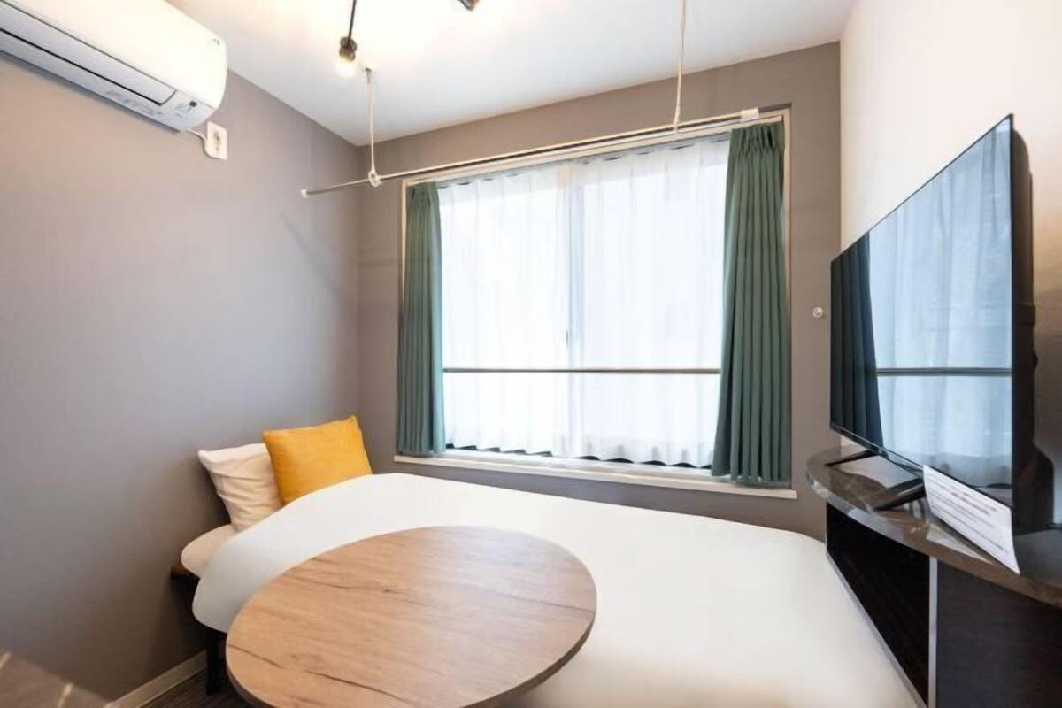 A hotel room with a bed, a round wooden table, a TV, and a window with curtains.