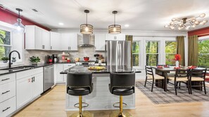 A modern kitchen with white cabinets, a central island, two black bar stools, and a dining area with a table and chairs.