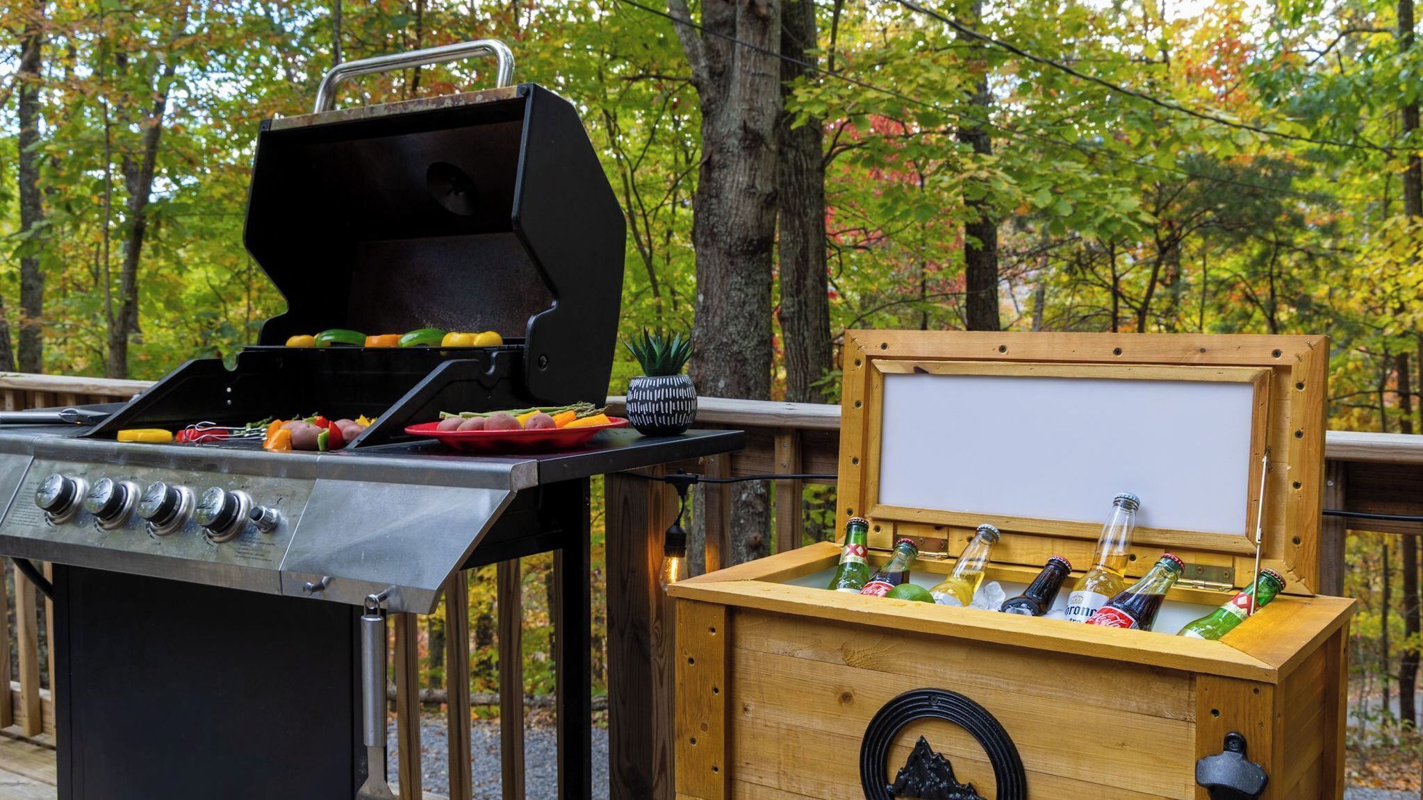 A barbecue grill with vegetables and a wooden box with bottles.