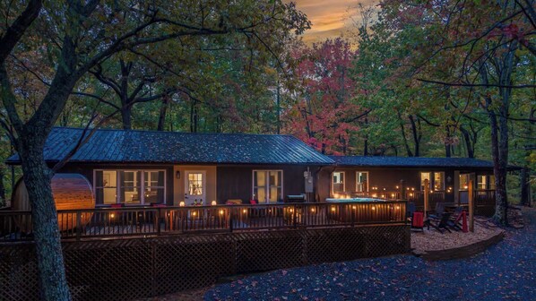 A cabin with a deck, large windows, and a hot tub.