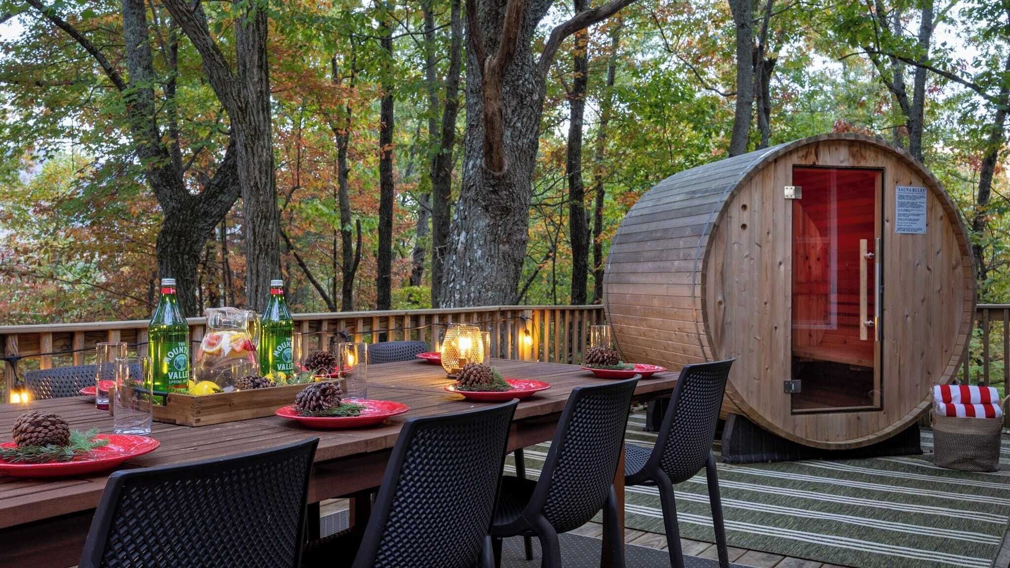 A wooden deck with a dining table set for two, surrounded by chairs, and a wooden barrel structure with a red door.