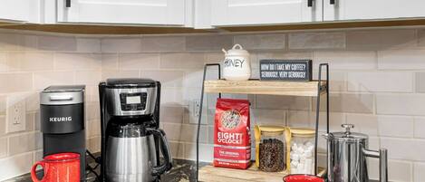 A kitchen with a Keurig coffee maker, a coffee pot, a mug, a sign, a bag of Eight O'Clock coffee, a honey jar, and a sugar container.