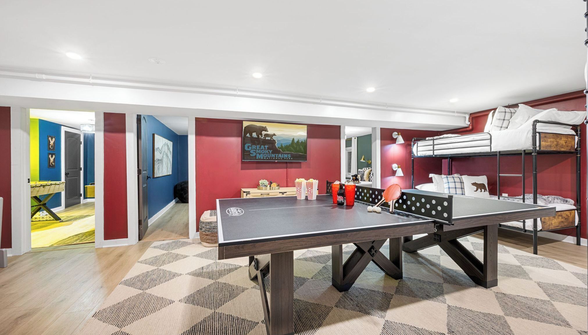 Une pièce avec une table de ping-pong, des lits superposés, un canapé et un mur orné d’une illustration d’un ours.