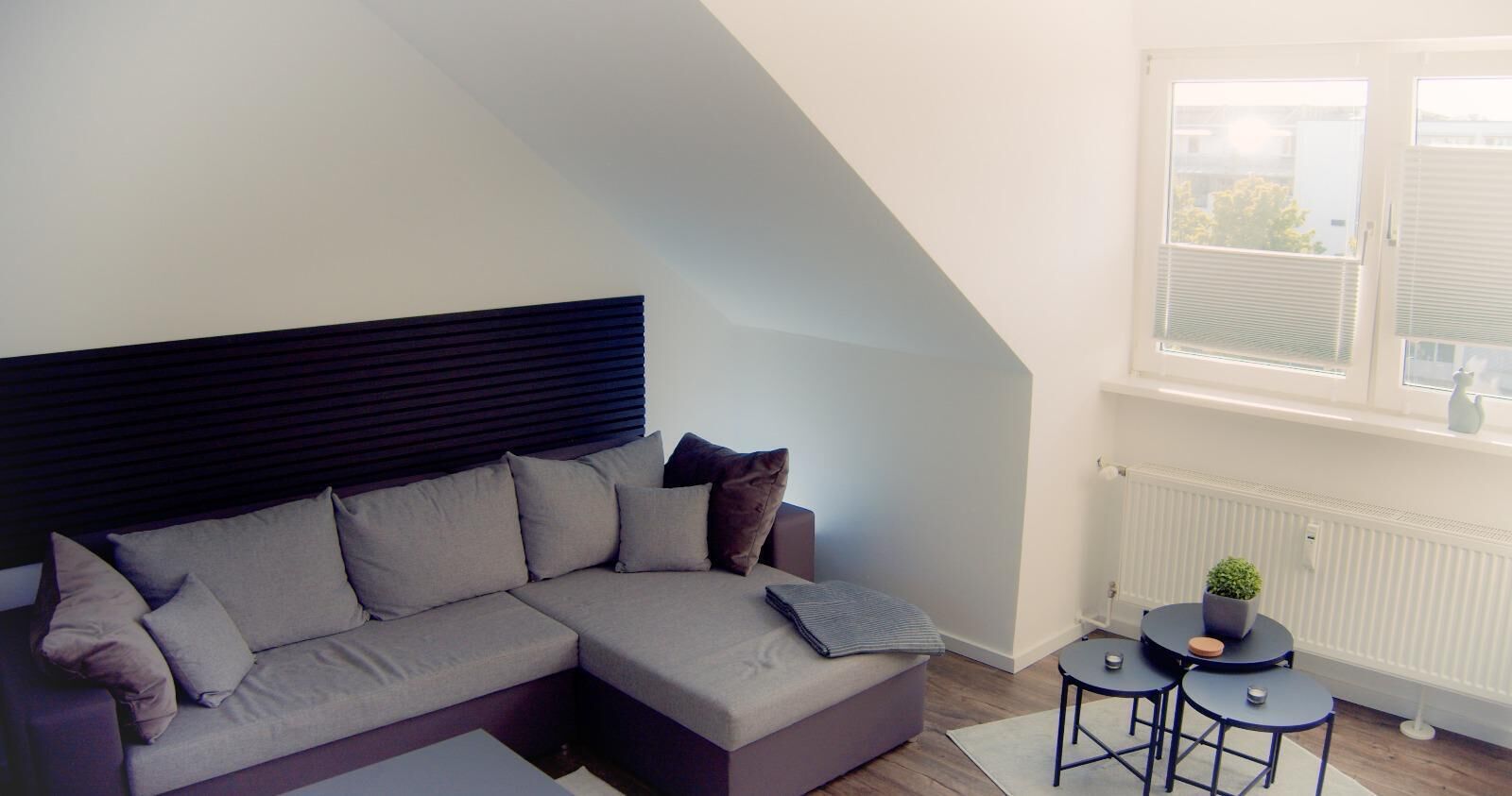 Ein modernes Wohnzimmer mit einer Eckcouch, einem runden Couchtisch und einem kleinen Beistelltisch mit Pflanze.