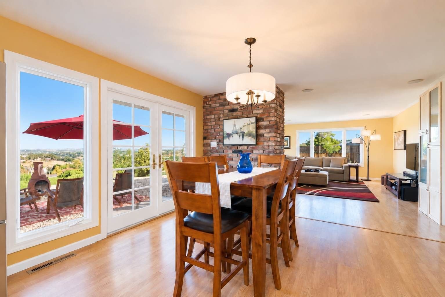 A dining area with a brick wall, a chandelier, and a view through large glass doors.