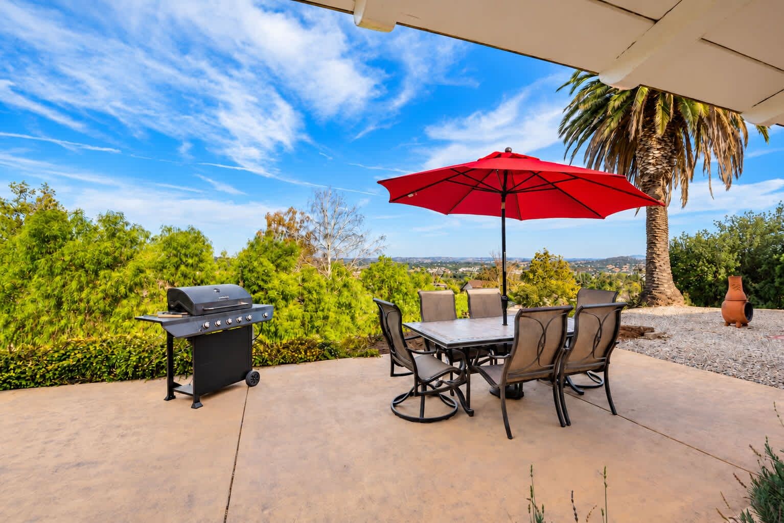 An outdoor patio with a grill, table, chairs, and a red umbrella.