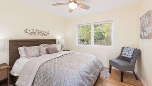 Une chambre à coucher comprenant un lit, une chaise, un ventilateur de plafond, une fenêtre et un élément de décoration murale.