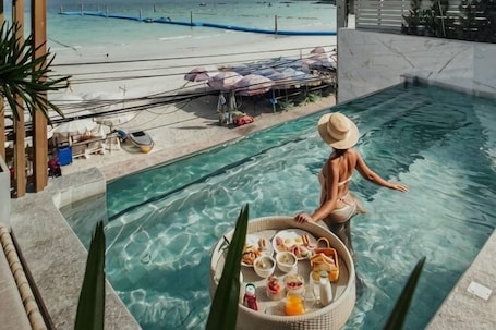 A poolside view with a dining setup, a beach, and umbrellas.. Mila Kohlarn