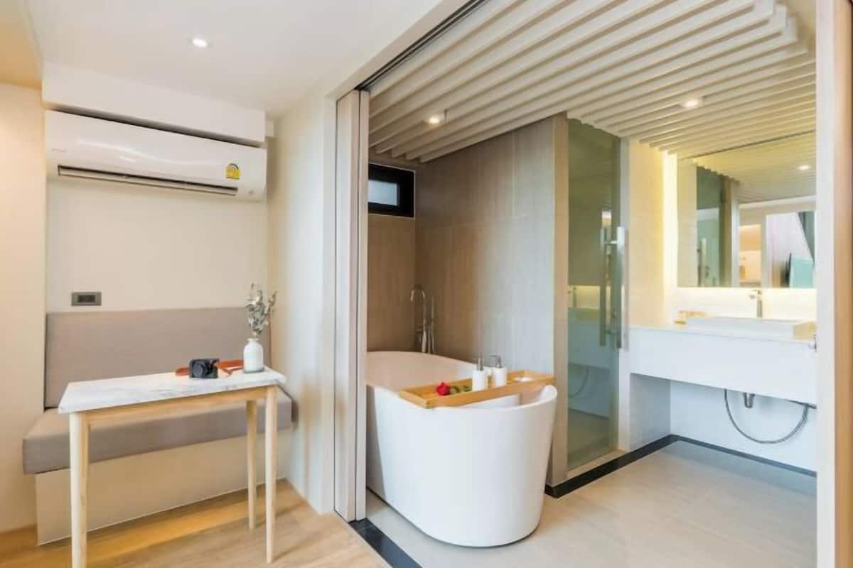 A modern bathroom with a freestanding bathtub, a vanity with a mirror, and a table with a vase and a book.