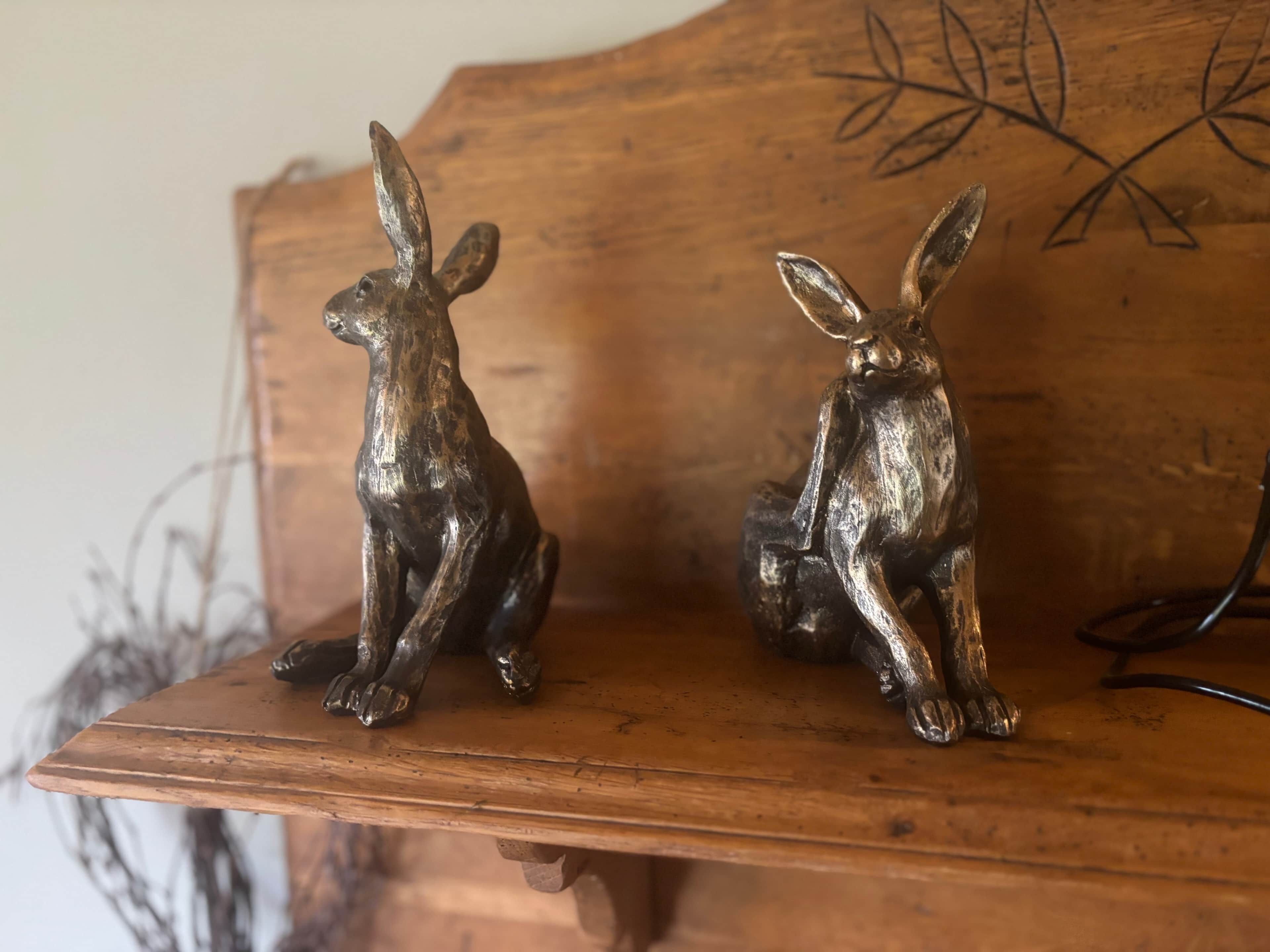 Two bronze rabbit sculptures on a wooden shelf.