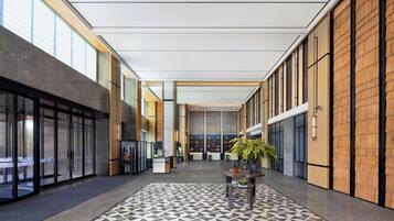 Un vestíbulo amplio con un piso de diseño geométrico, una mesa de recepción y una planta grande en el centro.