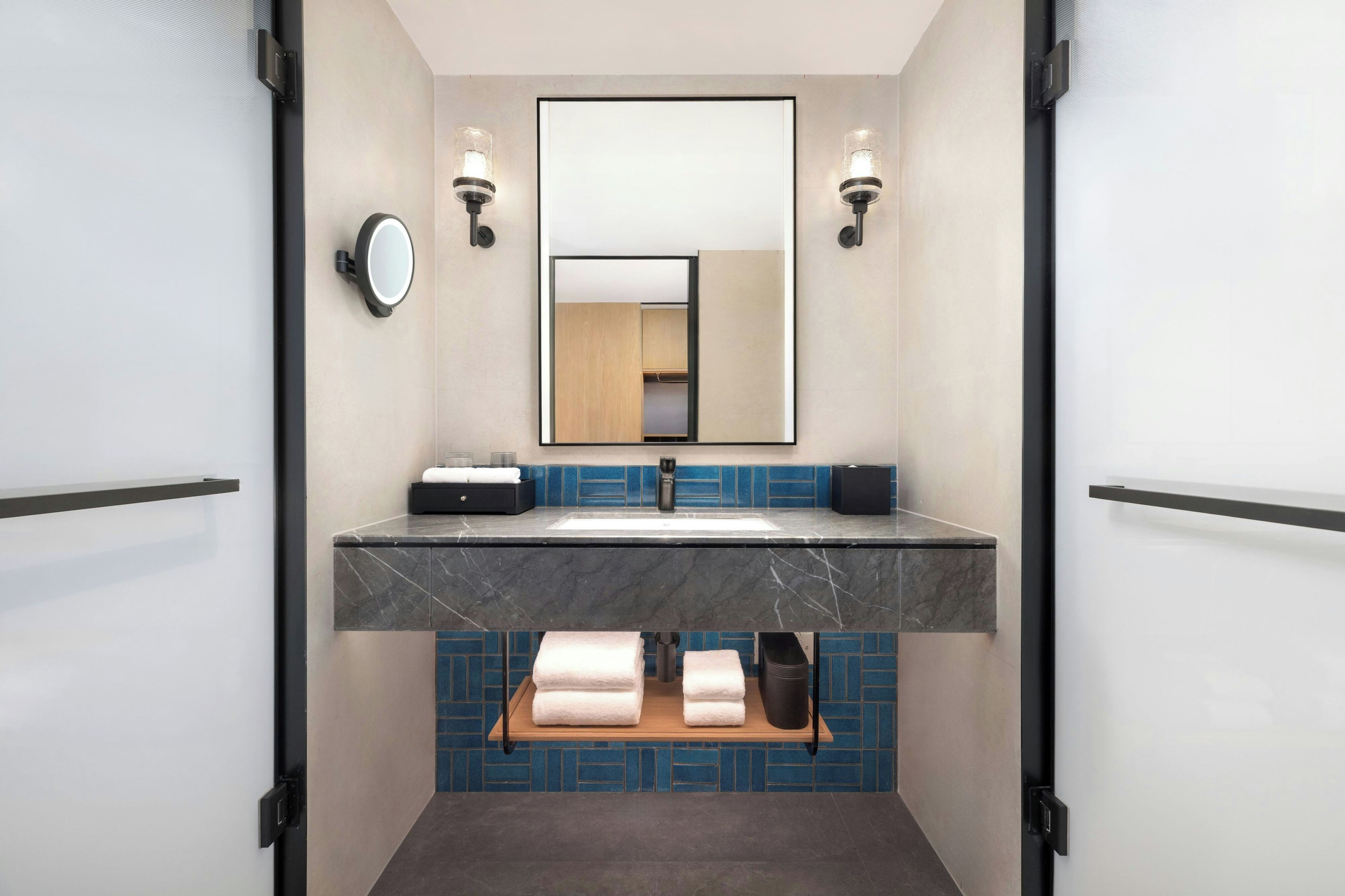 A modern bathroom with a marble sink, a mirror, and a blue tiled backsplash.