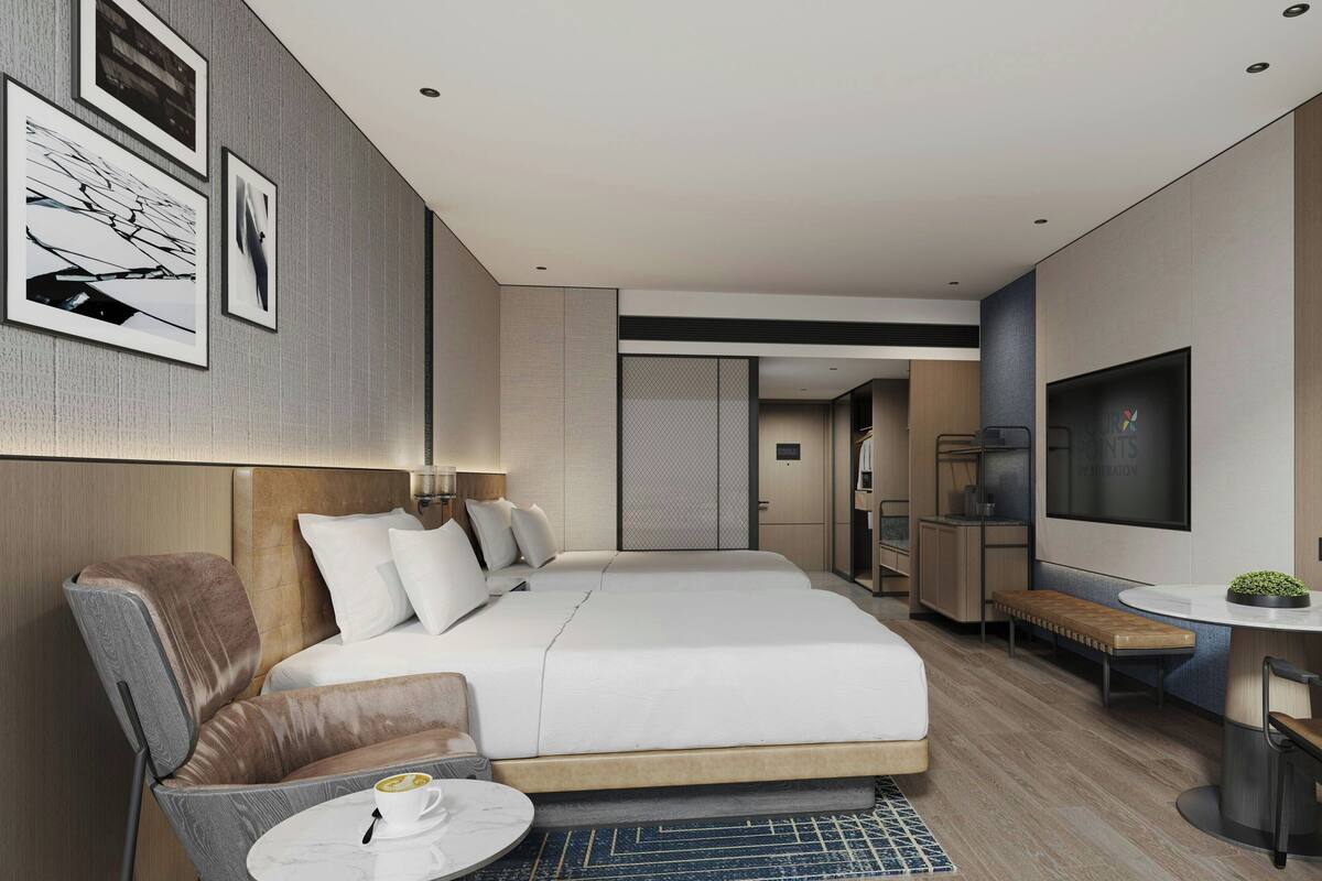 A modern hotel room with a large bed, a seating area with a coffee table, and a TV on the wall.