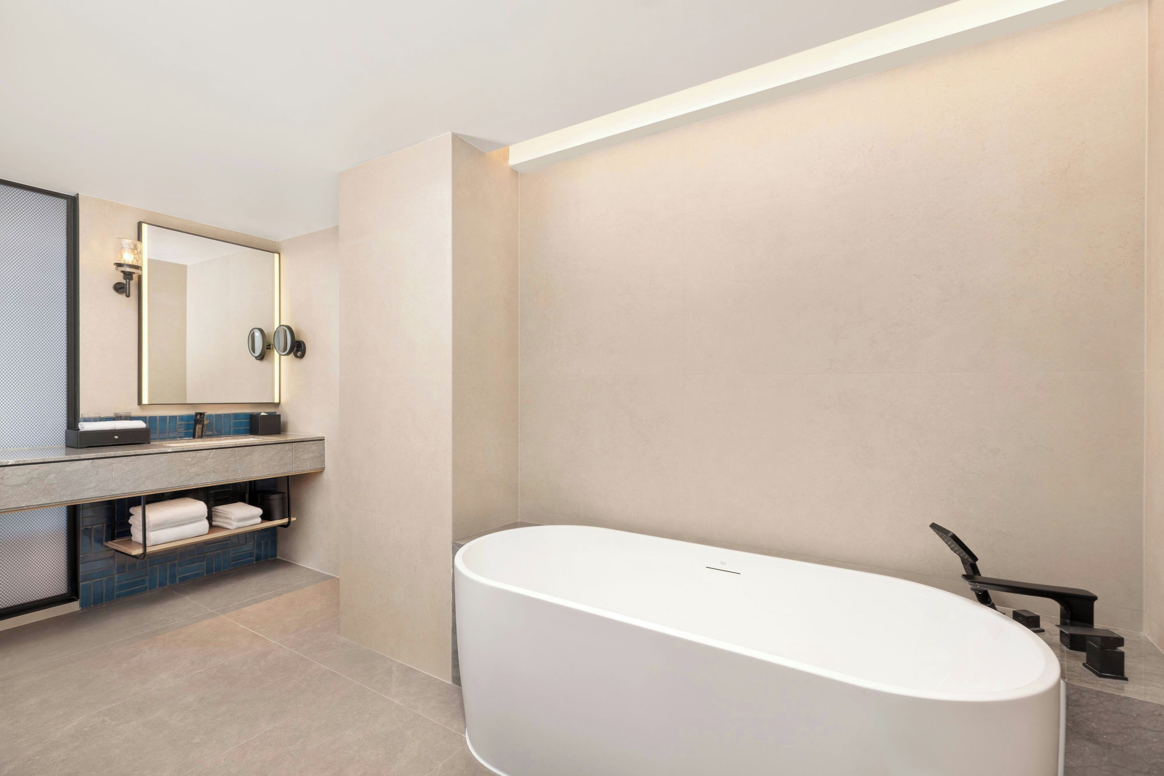 A modern bathroom with a freestanding bathtub, a large mirror, and a built-in vanity with shelves.