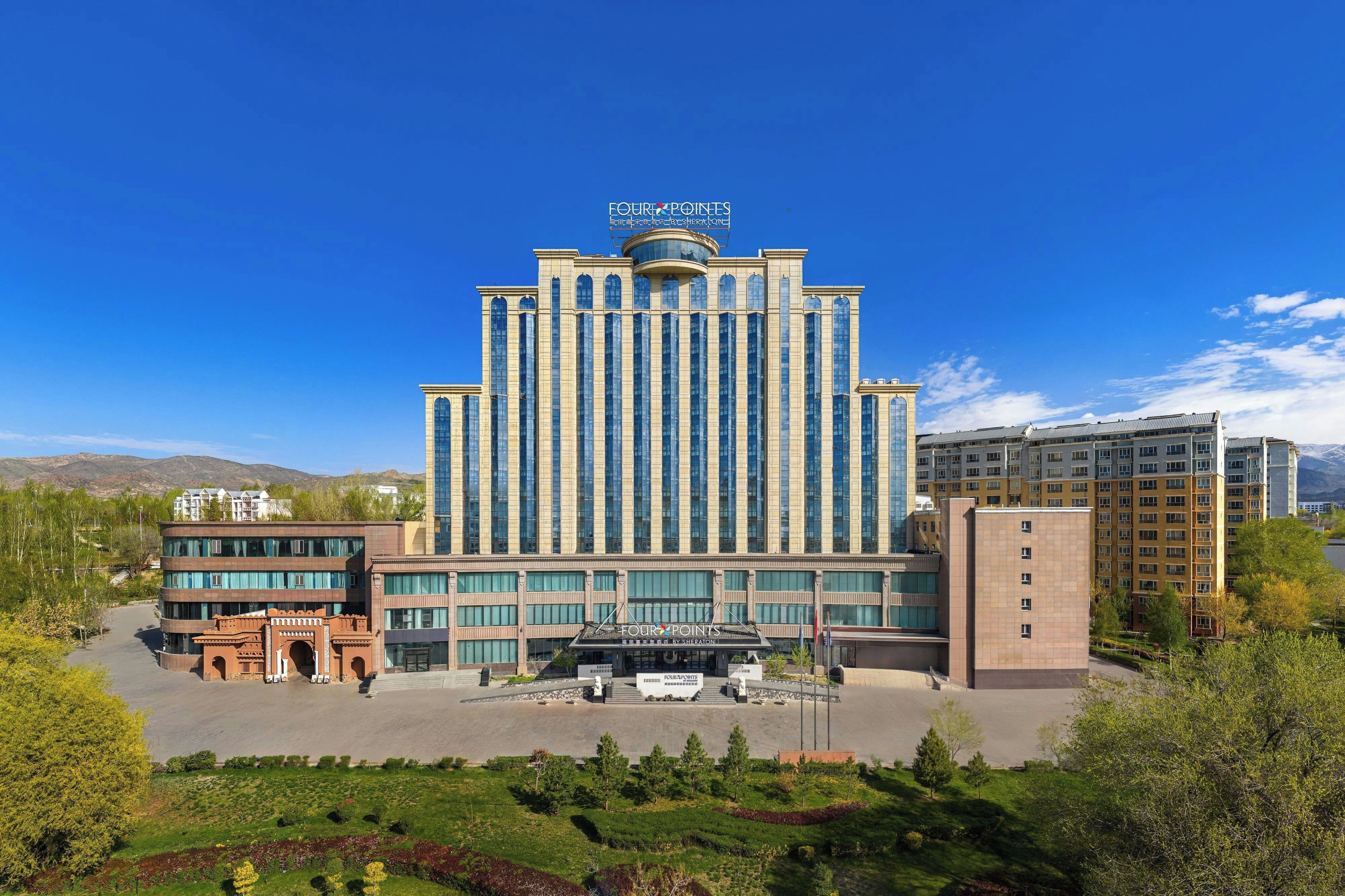 Een hotel met een centraal torentje, meerdere verdiepingen en een aangelegde voortuin.