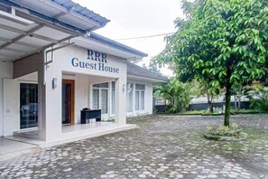 Een gebouw met de naam 'RRR Guest House', voorzien van een overdekte ingang en een geplaveid binnenterrein.