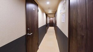 A long, narrow hallway with dark wooden doors on both sides, a tiled floor, and a ceiling with recessed lighting. - Jing House Akihabara Ryokan (Tokyo)
