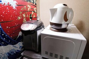 Eine Kaffeemaschine und eine digitale Waage stehen auf einem weißen Gerät, wahrscheinlich einer Mikrowelle, vor einem Stoff mit Muster.