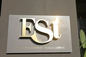 Een bord met de tekst 'ESTABLISHMENT - KUALA LUMPUR' op een grijze achtergrond.