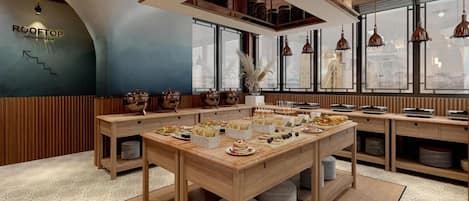 Un restaurante con techo alto, vigas de madera y una mesa central llena de comida y bebidas.