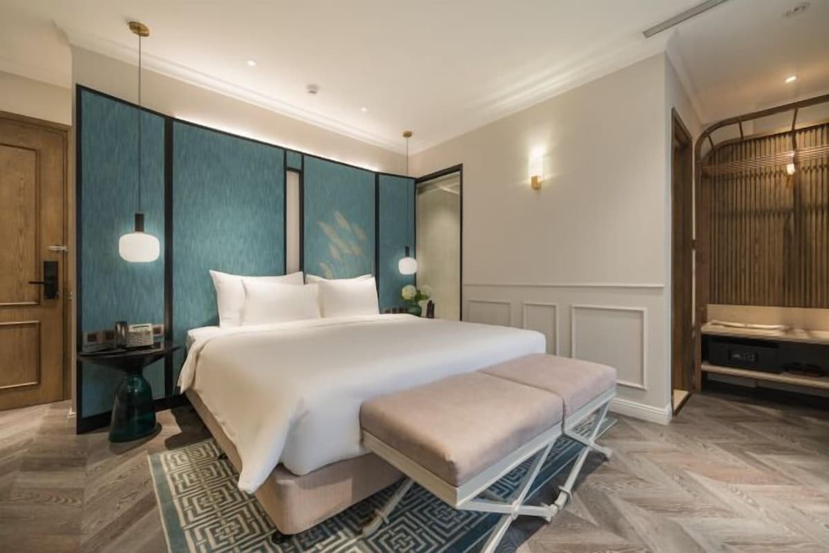 A modern hotel room with a large bed, bedside tables, a bench, and a wardrobe.