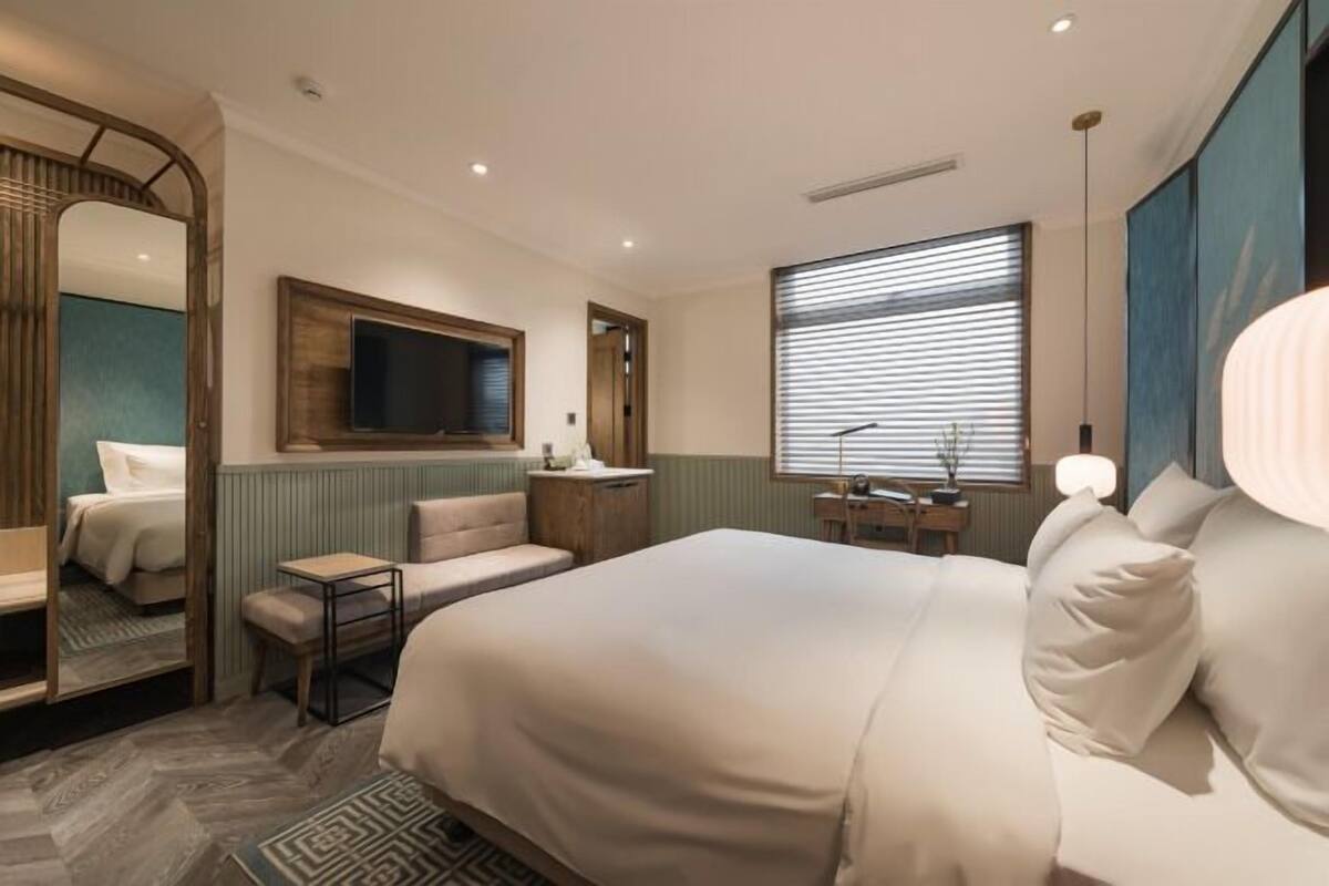 Ein Hotelzimmer mit einem großen Bett, einem Schreibtisch, einem Stuhl, einem Spiegel und einem Fernseher.