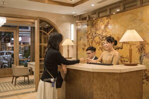 A reception desk with a wooden counter, a receptionist, and a guest.