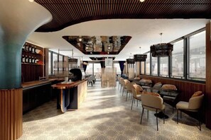 Un espace bar moderne doté d’un haut plafond, de tabourets et d’un coin salon avec des chaises.