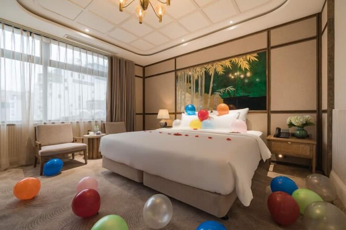 Ein Hotelzimmer mit einem großen Bett, einem Sessel, einem Nachttisch, einer Lampe und einer Wand mit einem tropischen Wandbild.