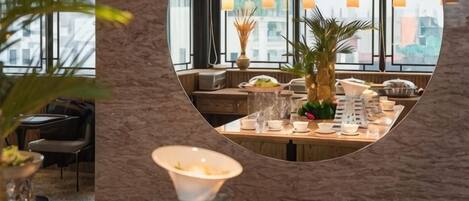 Een restaurant met een ronde spiegel die het interieur weerkaatst, een gedekte eettafel met borden en glazen, en een potplant.