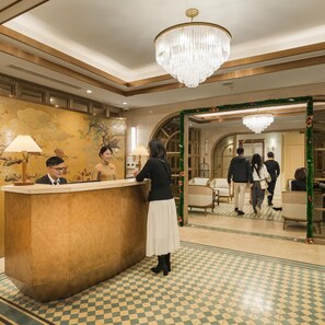A hotel reception area with a check-in counter, a chandelier, and a checkered floor pattern.