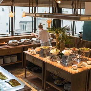 A breakfast buffet setup with various food items and a person serving. - La Passion Hanoi Hotel & Spa (Hanoi)