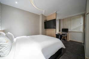 Een hotelkamer met een groot bed, een bureau met een computer en een aan de muur bevestigde televisie.