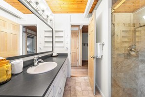 A bathroom with a sink, mirror, and shower. - Classic A-frame Cabin w/ Hot Tub + Deck & Easy Access Near Ski + Lake Summit Haven by Avantstay (Tahoe City)