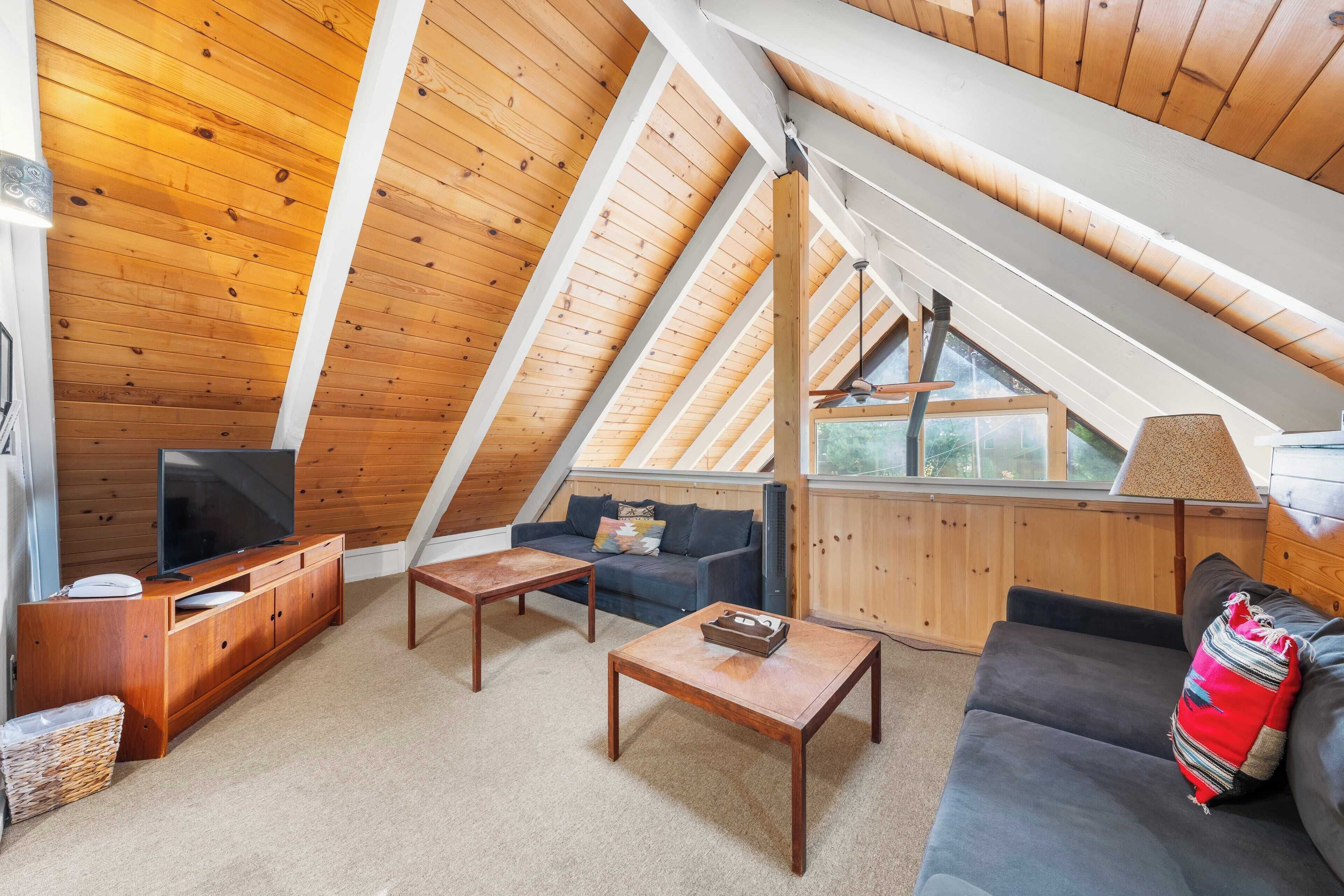 A cozy attic living room with a wooden ceiling, a TV, a sofa, and a coffee table.