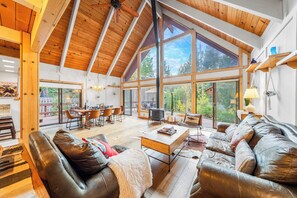 A spacious living area with a high ceiling, large windows, and a cozy seating arrangement. - Classic A-frame Cabin w/ Hot Tub + Deck & Easy Access Near Ski + Lake Summit Haven by Avantstay (Tahoe City)