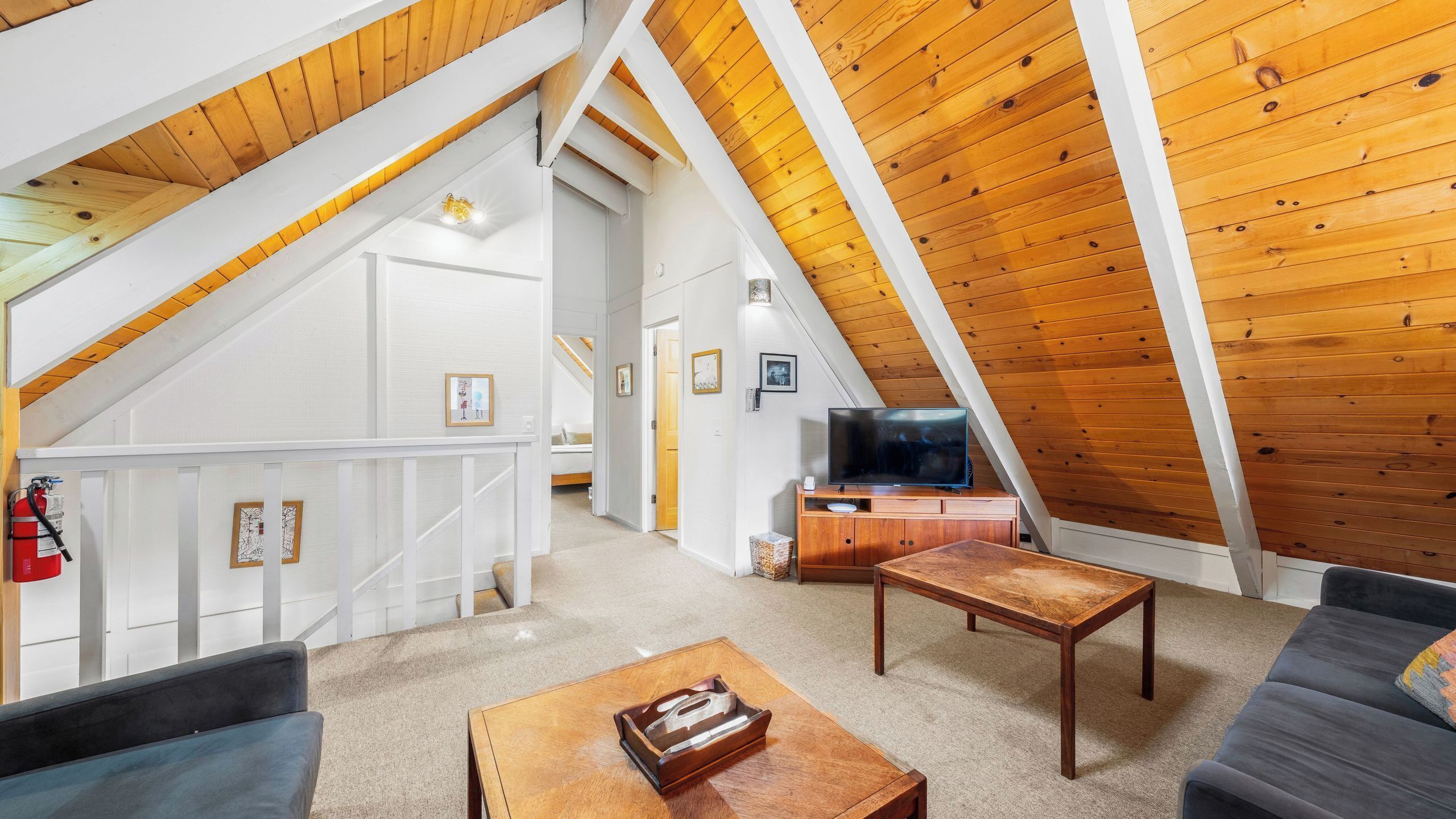 An attic living space with a wooden ceiling, a television, a sofa, and a coffee table.