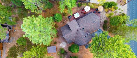 An aerial view of a residential area with a house featuring a sloped roof, a deck with outdoor furniture, and surrounding greenery.