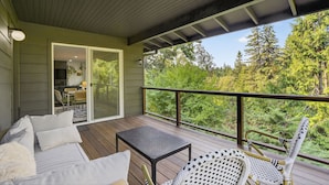 A covered deck with a sofa, table, and chairs, overlooking a forested area. - Modern Urban Retreat, Game Room (Portland)