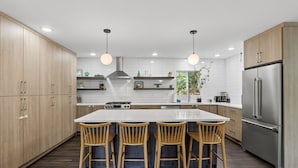 A modern kitchen with wooden cabinets, a central island with bar stools, stainless steel appliances, and pendant lighting. - Modern Urban Retreat, Game Room (Portland)