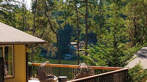 Une terrasse en bois avec deux fauteuils en osier et une petite table, d’où l’on a vue sur une zone boisée, un lac et un chalet au loin.
