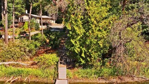 Une jetée en bois s’étendant sur une étendue d’eau, entourée d’une végétation luxuriante et avec une maison en arrière-plan.