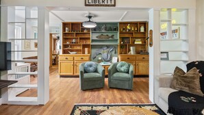 A spacious living room with a wooden floor, two green armchairs, a sofa with a black throw, and a bookshelf labeled "LIBERTY". - Walk Downtown! SUNY, near Power Plants, Hospital, Pets. 3 bathrooms, King beds! (Oswego)