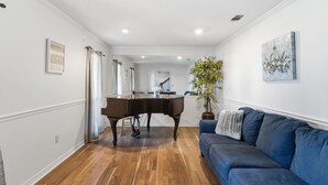 Un salon avec un grand piano, un canapé bleu, un parquet en bois et un escalier menant à une autre pièce.