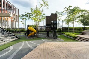 A playground with a slide and climbing structures, surrounded by a landscaped area with pathways and a building in the background. - Harmony Luxury Suites At Lucentia Bukit Bintang City Center (Kuala Lumpur)