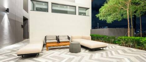 A modern outdoor lounge area with a herringbone-patterned floor, a sofa set, and a tree.