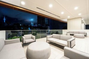 A modern lounge area with sofas and a round table, large windows with a city view, and a glass railing. - Harmony Luxury Suites At Lucentia Bukit Bintang City Center (Kuala Lumpur)