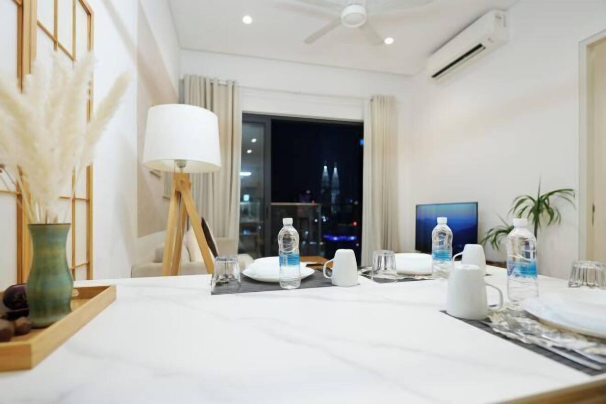 Ein Hotelzimmer mit Esstisch für zwei Personen, einer Lampe, einem Fernseher und Blick auf die beleuchtete Stadt.