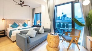 A modern hotel room with a bed, sofa, dining table, and chairs, a balcony with a city view, and a ceiling fan. - Harmony Luxury Suites At Lucentia Bukit Bintang City Center (Kuala Lumpur)